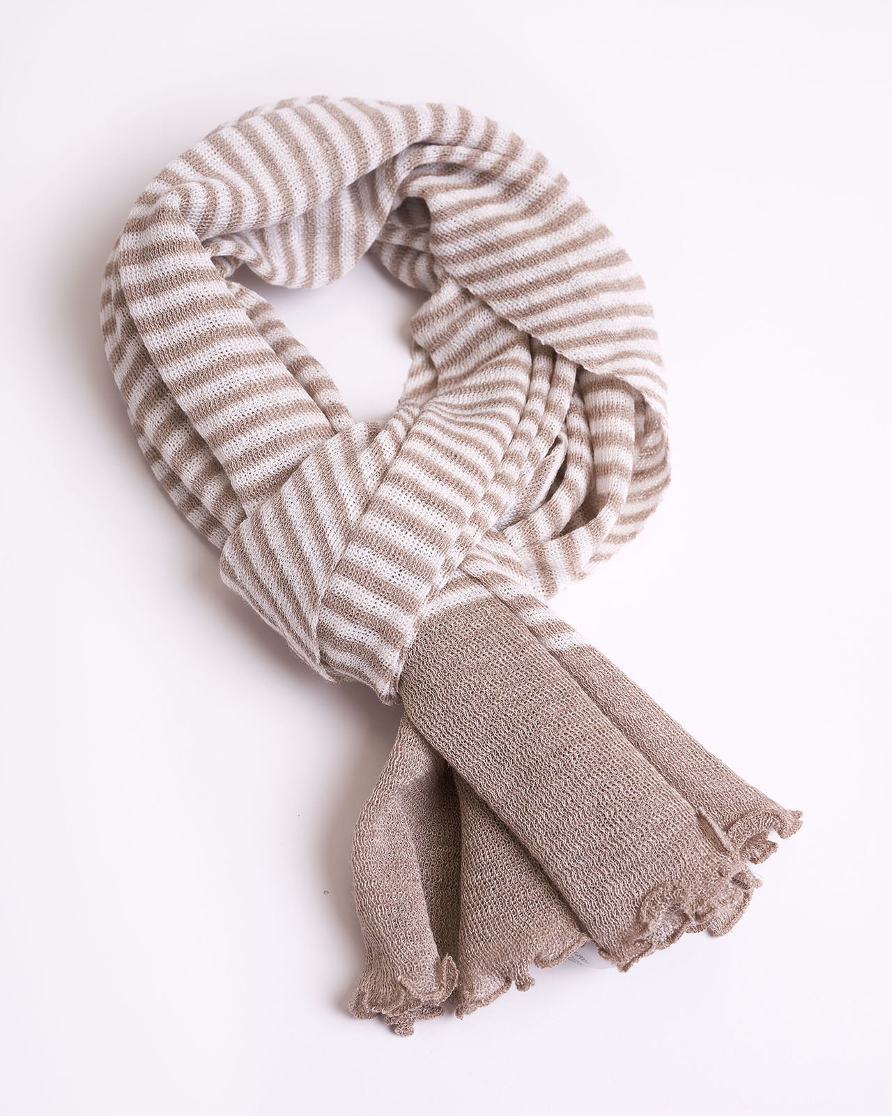 Soft textured linen scarf arranged in a loose knot, featuring a delicate beige and white striped pattern with subtle textural details. The ends of the scarf have a frayed, fuzzy finish, adding a casual yet elegant touch. The scarf is displayed against a white background, highlighting its cozy and inviting appearance